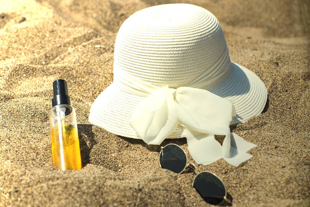 White hat, suntan lotion and sunglasses on the natural beach sand, close up - Photo, Image