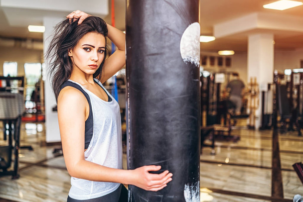 Pretty sporty girl near punching bag in gym - Fotó, kép