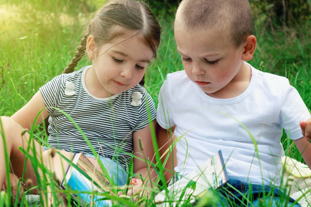 Kinder sitzen an einem sonnigen Tag auf dem Rasen und lesen ein Buch - Foto, Bild