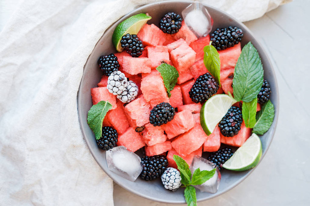 Fruit salad from Watermelon slices, frozen blackberry and lime on a plate on white background. Top view - Φωτογραφία, εικόνα