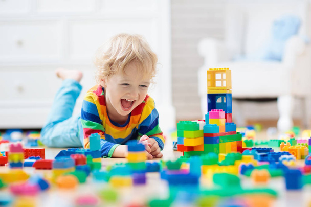 カラフルなおもちゃのブロックで遊ぶ子供。自宅やデイケアで小さな男の子の建物の塔。幼い子供のための教育玩具。赤ちゃんや幼児の子供のための建設ブロック。幼稚園プレイルームでの混乱. - 写真・画像