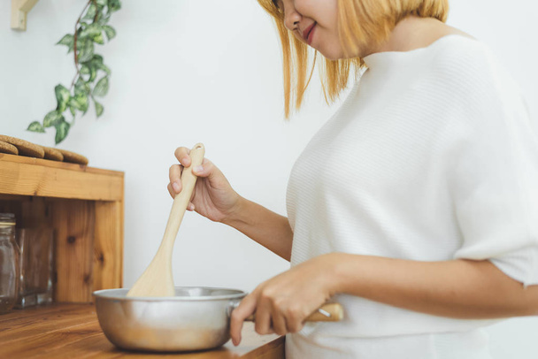 Азиатская женщина делает здоровую пищу стоя счастливо улыбаясь на кухне, готовит салат. Веселая азиатская молодая женщина дома. Здоровое питание и здоровый образ жизни приготовления пищи в домашних условиях Концепция
. - Фото, изображение