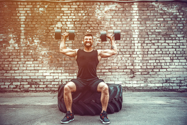 Muscular guy doing exercises with dumbbell against a brick wall - Φωτογραφία, εικόνα