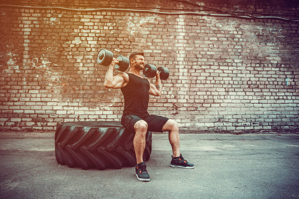 Muscular guy doing exercises with dumbbell against a brick wall - Fotografie, Obrázek