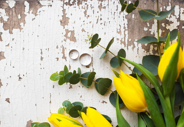 обручальные кольца с желтыми тюльпанами на старом белом столе
 - Фото, изображение