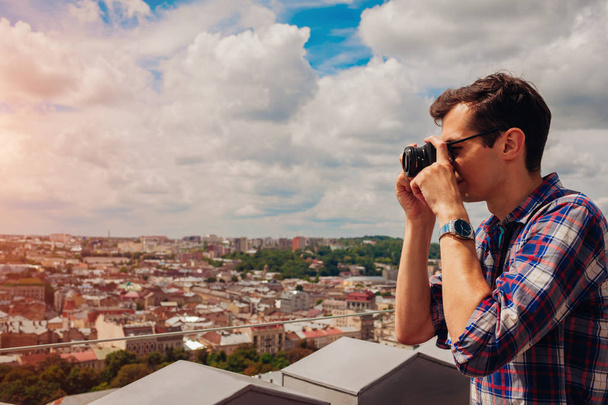 Πορτρέτο του χαρούμενος νεαρός άνδρας, τουρίστας με κάμερα λαμβάνει εικόνες των παλαιών πόλης Λβιβ από άποψη. Καλοκαιρινές διακοπές - Φωτογραφία, εικόνα