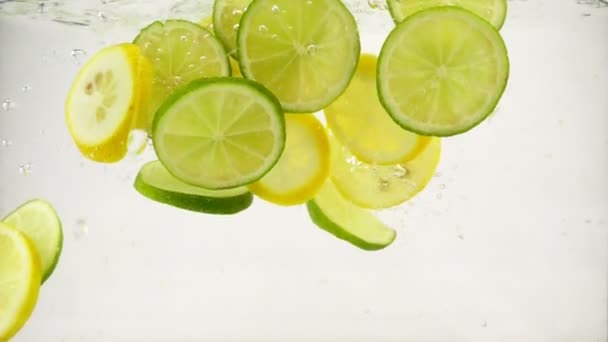 Limetten- und Zitronenscheiben fallen in ein Wasser mit Spritzern und Blasen, Zeitlupe in Großaufnahme - Filmmaterial, Video