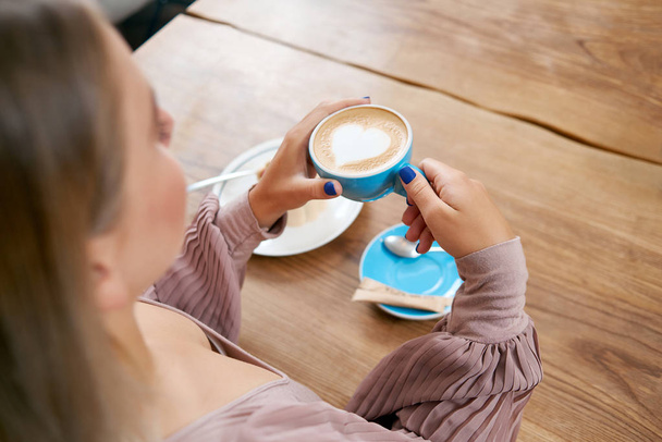 Fiatal lány tartás csésze kávé ül a fa tábla. - Fotó, kép