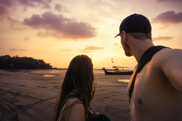 Pari seisoo Thaimaan rannalla ja katsoo kultaista violettia auringonlaskua.
 - Valokuva, kuva