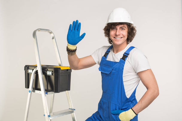 Studioporträt des gutaussehenden Bauunternehmers mit weißem Helm und blauem Overall beim Händeschütteln und Lachen. - Foto, Bild