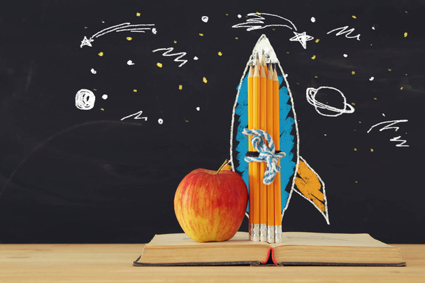 Back to school concept. rocket sketch and pencils over open book in front of classroom blackboard - Fotografie, Obrázek