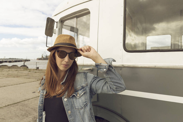 Beautiful day. Attractive young woman in hat standing by the travel van. Car travel, summer vacation and adventure - Photo, Image