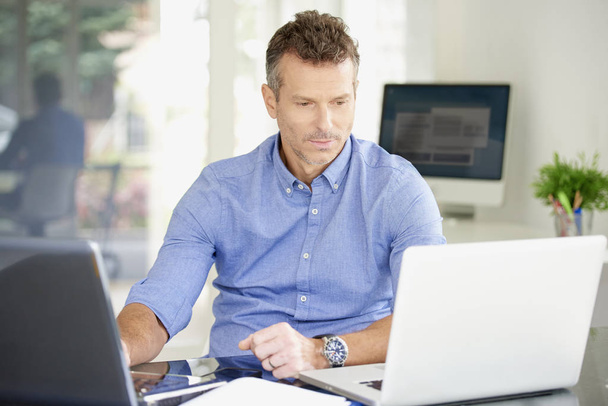 Thinking casual businessman using laptop while working on workstation at the office. Multitasking.  - Valokuva, kuva