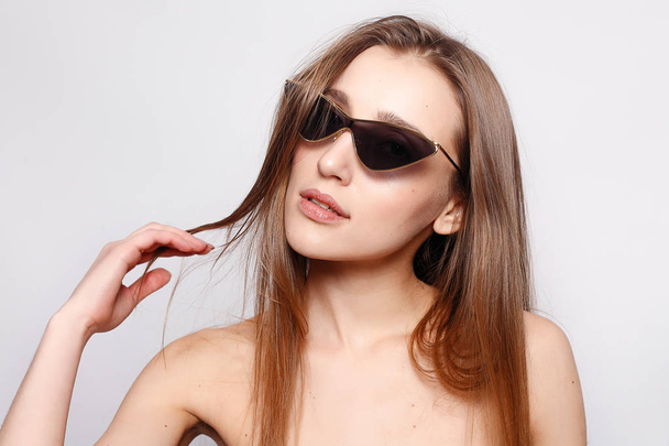 emotions, fashion, people, youth and beauty concept - Close up shot of stylish young woman in sunglasses smiling against gray background. Beautiful female model with copy space. - 写真・画像