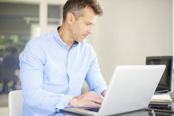 Středního věku podnikatel na sobě košili, zatímco sedí v kanceláři a používá svůj počítač.  - Fotografie, Obrázek