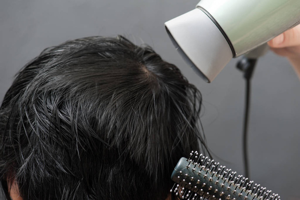 Drying black hair after dying. Hands, brush and hairdryer on background - Photo, Image