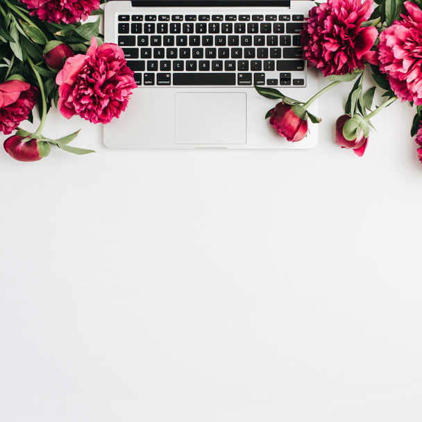 Minimale werkruimte met laptop en roze pioen bloemen op witte achtergrond. Plat lag, top uitzicht blog held kop. - Foto, afbeelding