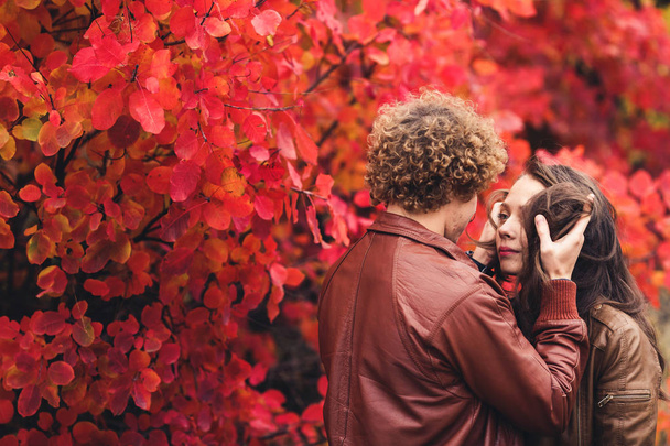 Hombre bigote de pelo rizado y mujer morena abrazándose en otoño contra el fondo de los árboles rojos
. - Foto, Imagen