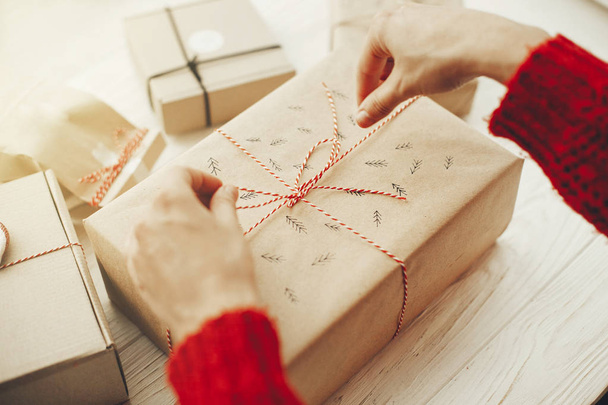 женские руки, заворачивающие стильные рождественские подарки с красной лентой. современные подарки ремесла на белом деревянном фоне. Счастливого Рождества. сезонные поздравления
 - Фото, изображение