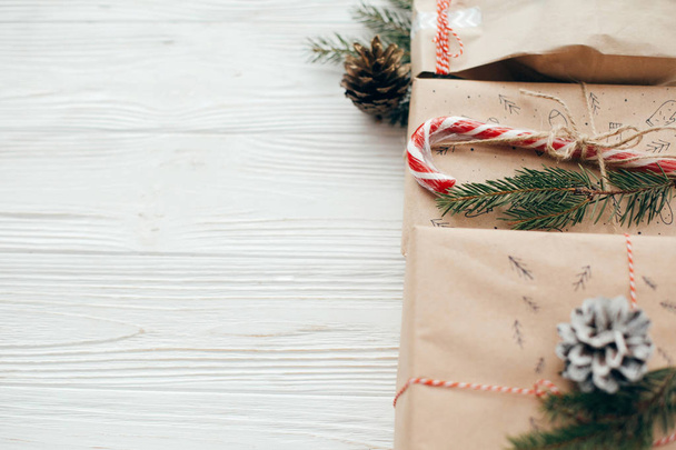 Joyeux Noël concept. cadeaux élégants avec ruban rouge, canne à bonbons, branches de pin, cônes. cadeaux d'artisanat moderne sur fond blanc en bois, espace pour le texte. salutations saisonnières
 - Photo, image