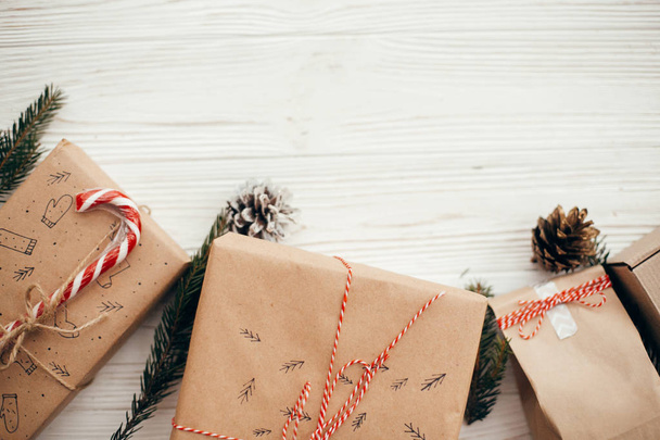 スタイリッシュなシンプルなクリスマスは、赤いリボン、キャンデー杖、松の枝、コーンを提示します。白い木製の背景、フラットの現代クラフト ギフトが横たわっていた。季節のグリーティング カード. - 写真・画像