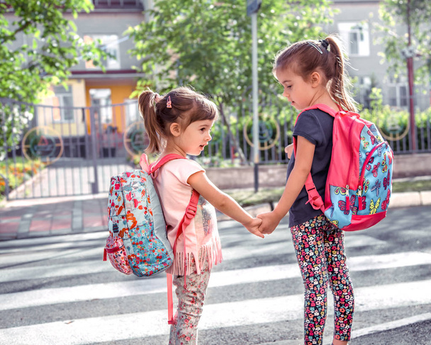 Діти ходять до школи, щасливі студенти зі шкільними рюкзаками і тримають руки разом, перетинають дорогу, концепція виховання з дівчатами
 - Фото, зображення