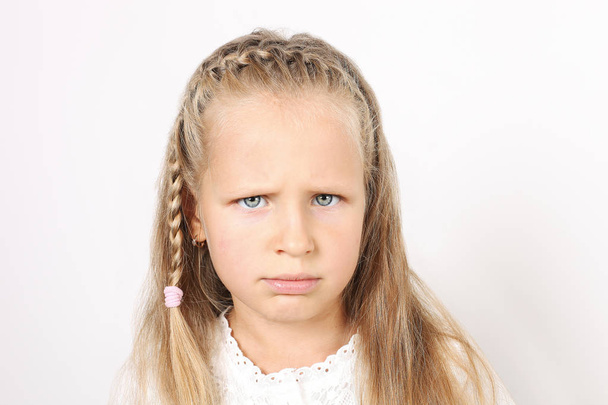 Portrait of sad and funny four year old little girl with blond hair, pigtail, dressed in white shirt, frowning dissatisfied facial expression. Child female, isolated background, copy space, close up. - Fotografie, Obrázek