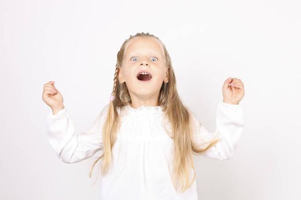 Portrait of positive and funny four year old little girl, blond hair, pigtail, dressed in white shirt celebrating win with raised arms. Child female hands up, isolated background, copy space, close up - Fotografie, Obrázek