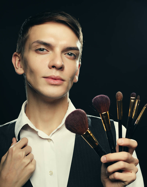 Ready to do make up. Young male make up artist posing with make-up brushes on a dark background - Photo, Image