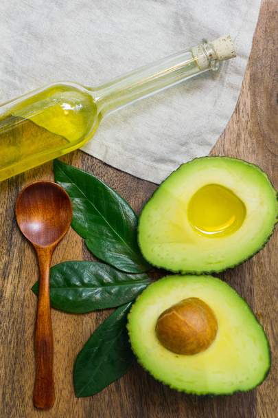 Avocado sliced with avocado leaves and avocado oil in a bottle on a wooden background - Fotoğraf, Görsel