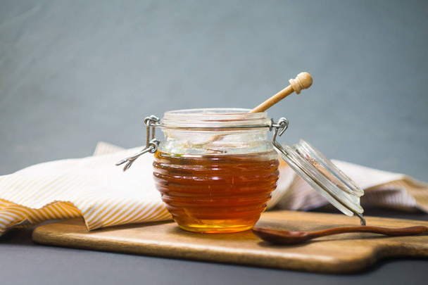Honey in a jar with a wooden honey dipper on a wooden board - Fotó, kép