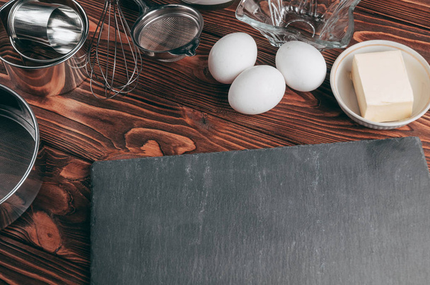 Los ingredientes en los platos sobre una mesa marrón de madera, donde también se encuentra el batidor está lleno de harina, tres huevos de pollo y una pizarra. Vista desde arriba. Colocar debajo del texto
 - Foto, Imagen