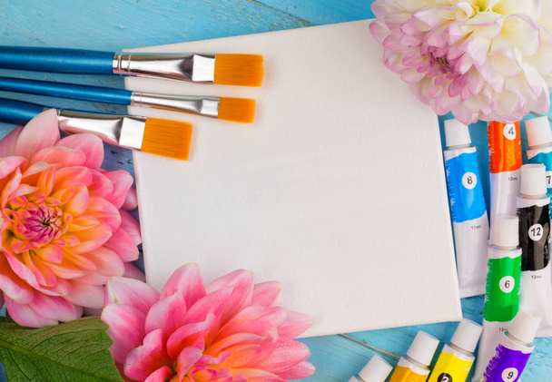 summer background. dahlias, paints, brushes and a canvas on a blue wooden background. art. space for a text - Photo, Image
