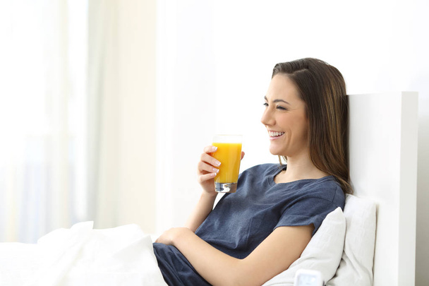 Boldog asszony feküdt egy ágyon gazdaság egy narancslé a reggeli otthon - Fotó, kép