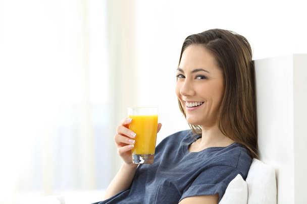 Happy woman looking at camera holding an orange juice for breakfast - Photo, image
