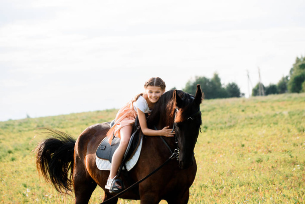 cute little girl on a horse in a summer field dress. sunny day. - Zdjęcie, obraz