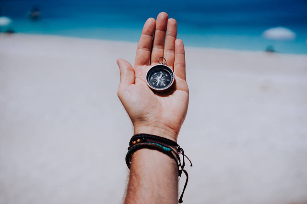 One open stretched hand palm with black metal compass on the sandy beach. Find your wish goal way concept. Blue sea in background. Point of view pov - Foto, Imagem