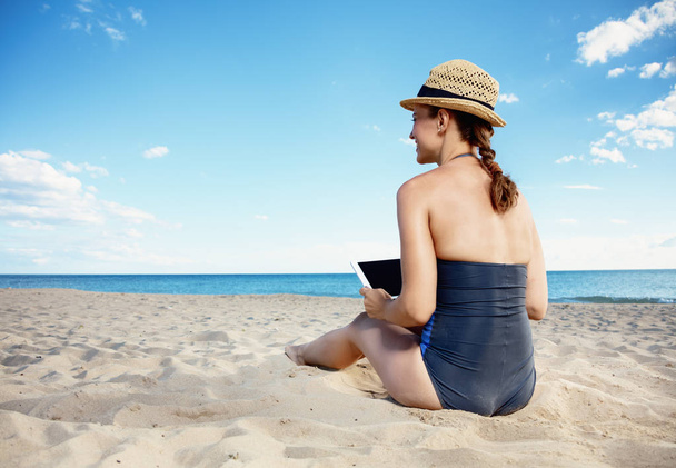 Seen from behind young woman in swimsuit with tablet PC on the seashore - Foto, Imagem