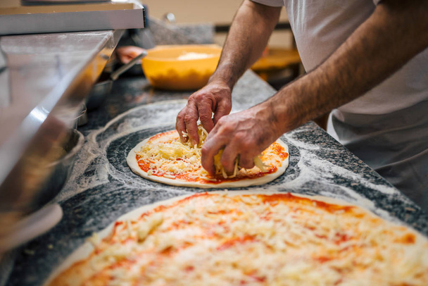 Chef in the kitchen putting the cheese on the pizza. - Photo, Image