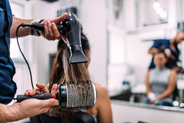 Close-up image of hairdressers hands drying long hair with blow dryer and round brush. - Fotó, kép