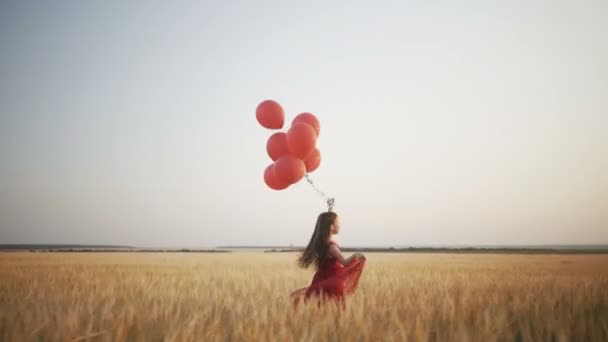 šťastná mladá dívka s balóny, které jsou spuštěny v poli pšenice při západu slunce - Záběry, video