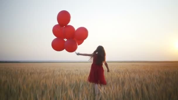 glückliches junges Mädchen mit Luftballons im Weizenfeld bei Sonnenuntergang - Filmmaterial, Video