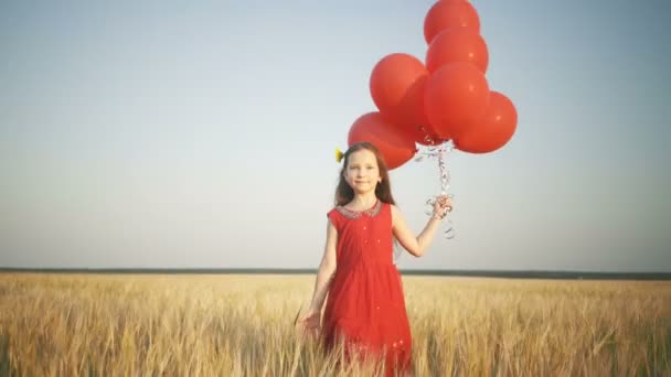 šťastná mladá dívka s balóny, které jsou spuštěny v poli pšenice při západu slunce - Záběry, video