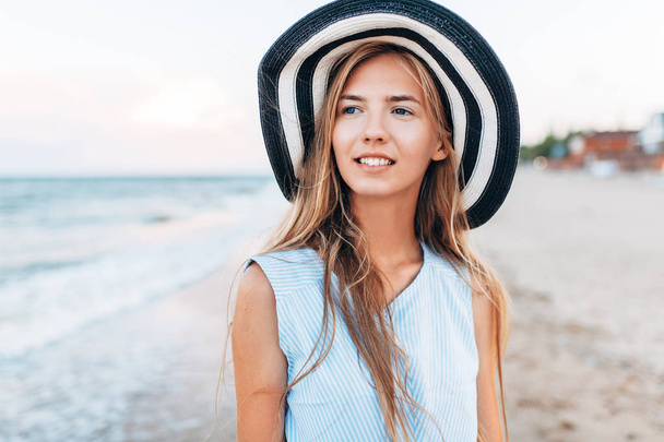 帽子のクローズ アップの女の子の美しい肖像画残り、海または海に夏の青いドレスを着た女性 - 写真・画像