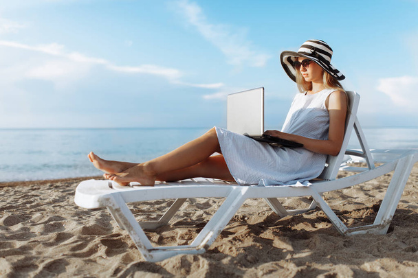 Beautiful girl sitting with a laptop on a chaise longue, a woman working on vacation - Photo, Image