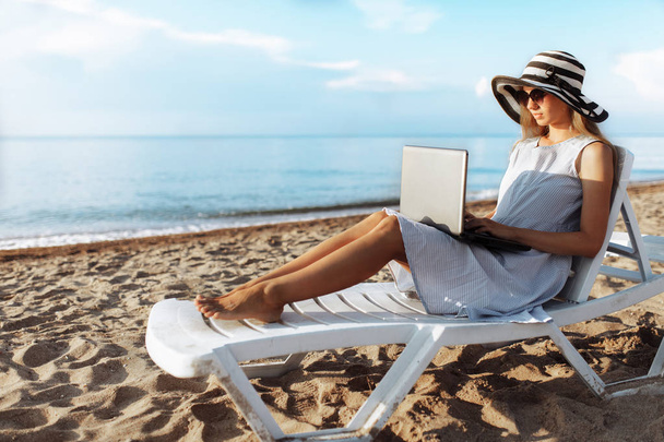 Beautiful girl sitting with a laptop on a chaise longue, a woman working on vacation - Fotoğraf, Görsel