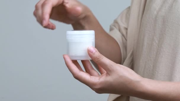 Close-up of woman's hands opening a jar with cream on the white background. The container is held vertically. - Felvétel, videó