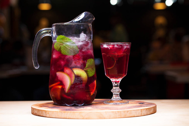 Homemade red wine sangria with orange, apple, strawberry and ice in glass and pitcher - Fotografie, Obrázek