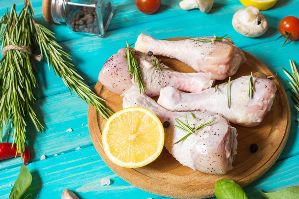 Raw uncooked chicken legs, drumsticks on blue wood background, meat with ingredients for cooking - Fotó, kép