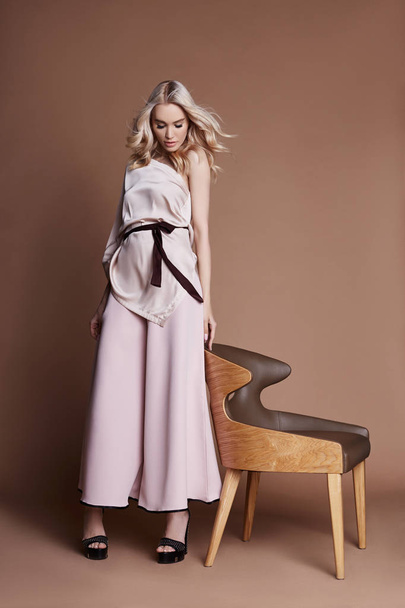 Sexy luxurious woman in a dress sitting on a chair. Autumn collection of women clothing. Fashion blonde in a long beautiful dress posing on background. Beautiful hair and a perfect girl figure - 写真・画像